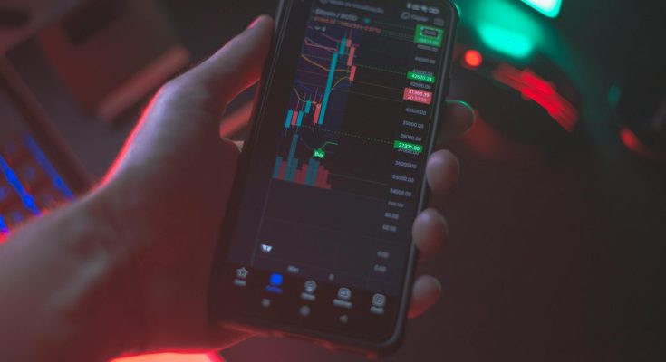 Hand holding smartphone displaying cryptocurrency trading app with financial data.