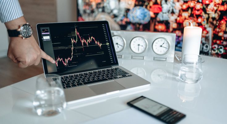 Businessman pointing at a financial graph on a laptop screen, showcasing stock market analysis.
